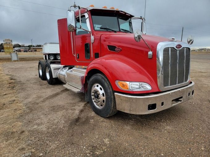 A red semi truck is parked in a dirt field.