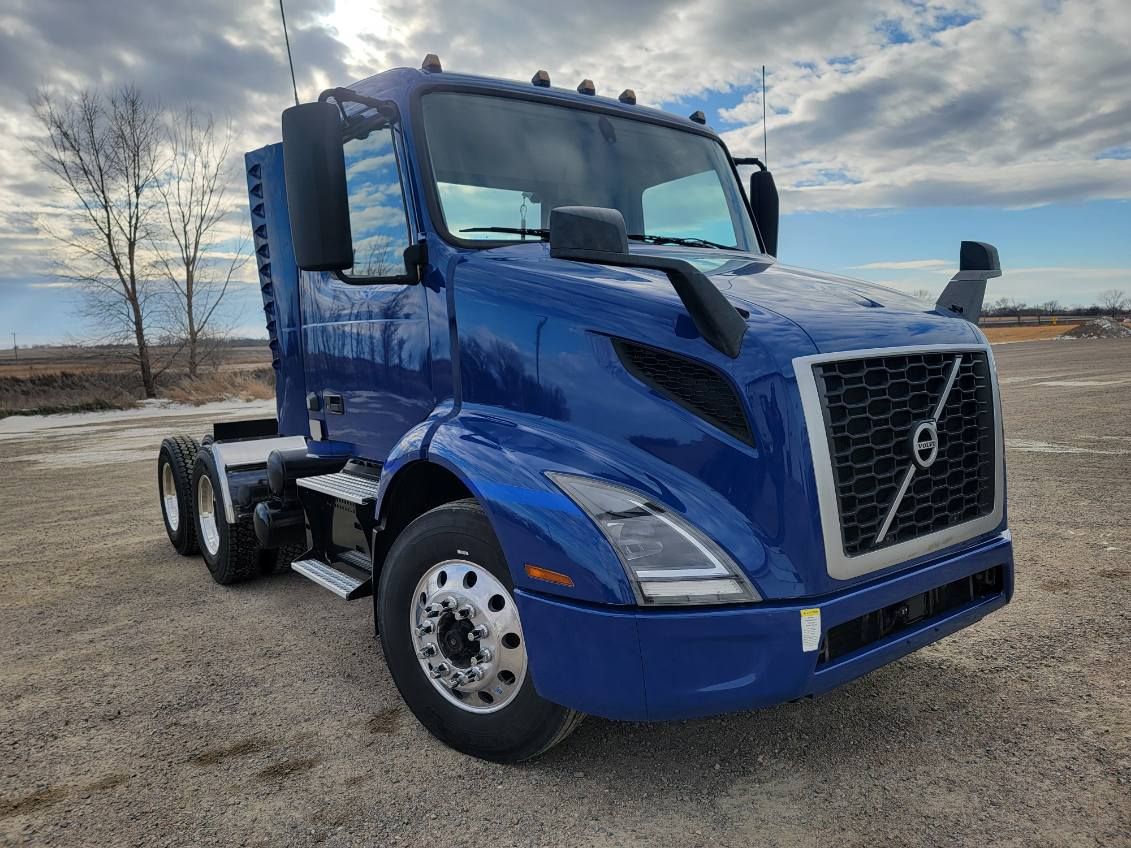A blue volvo semi truck is parked in a dirt field.