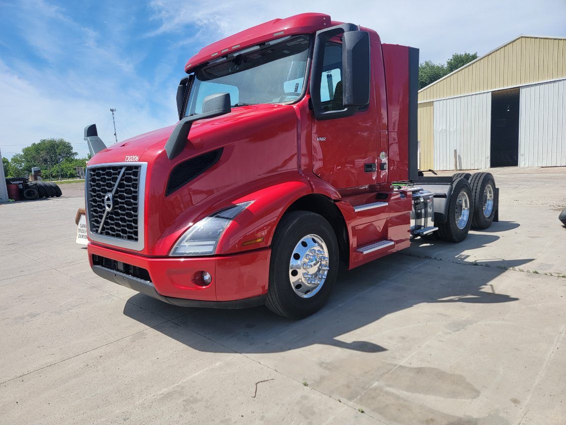 A red semi truck is parked in a parking lot in front of a building.