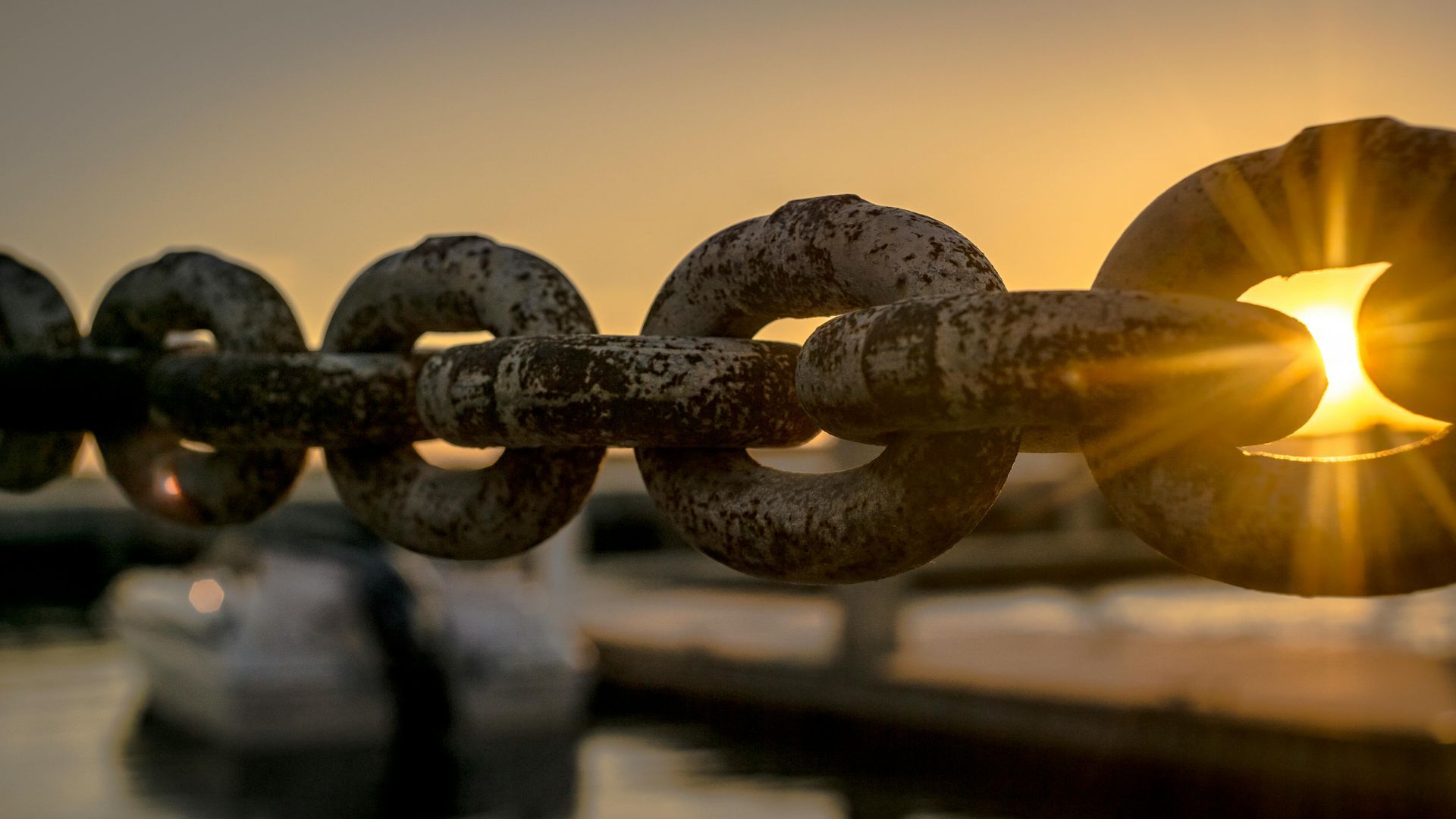 A close up of a rusty chain with the sun shining through it.