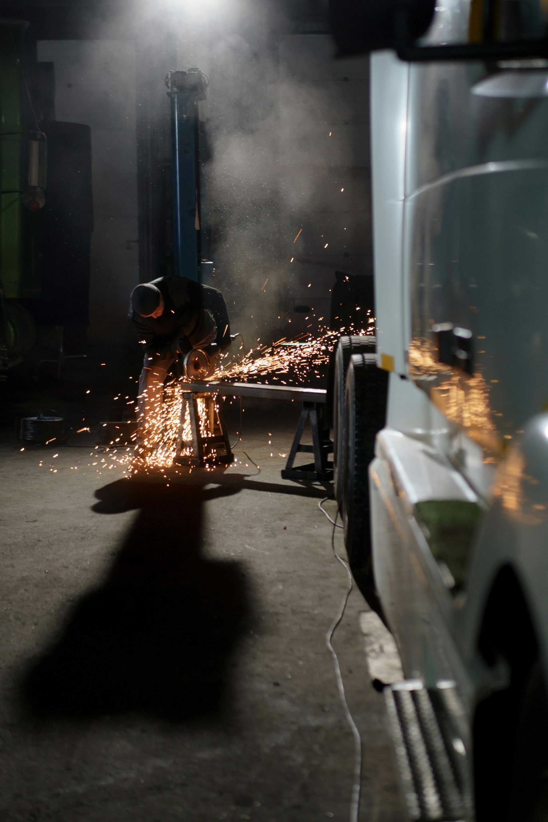 A man is welding a piece of metal in a garage at night.