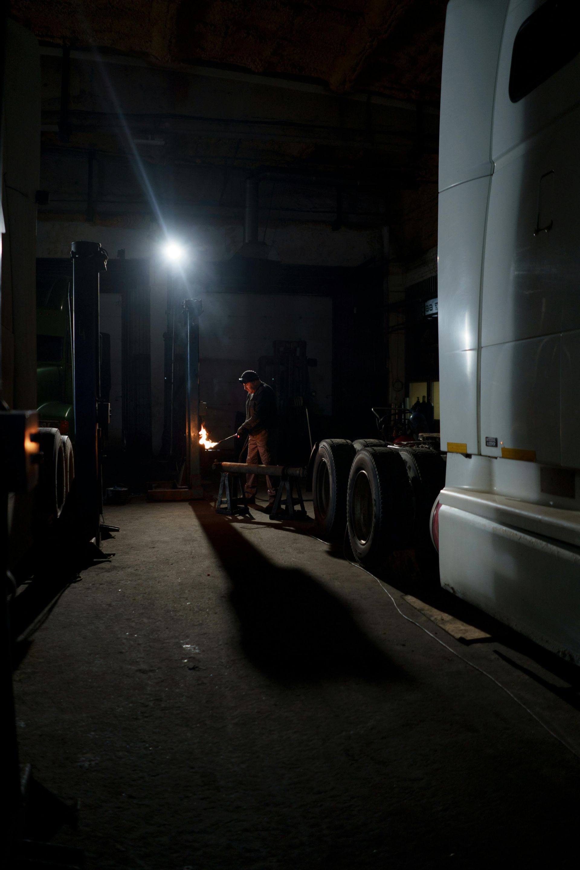 A man is working on a truck in a dark garage at night.