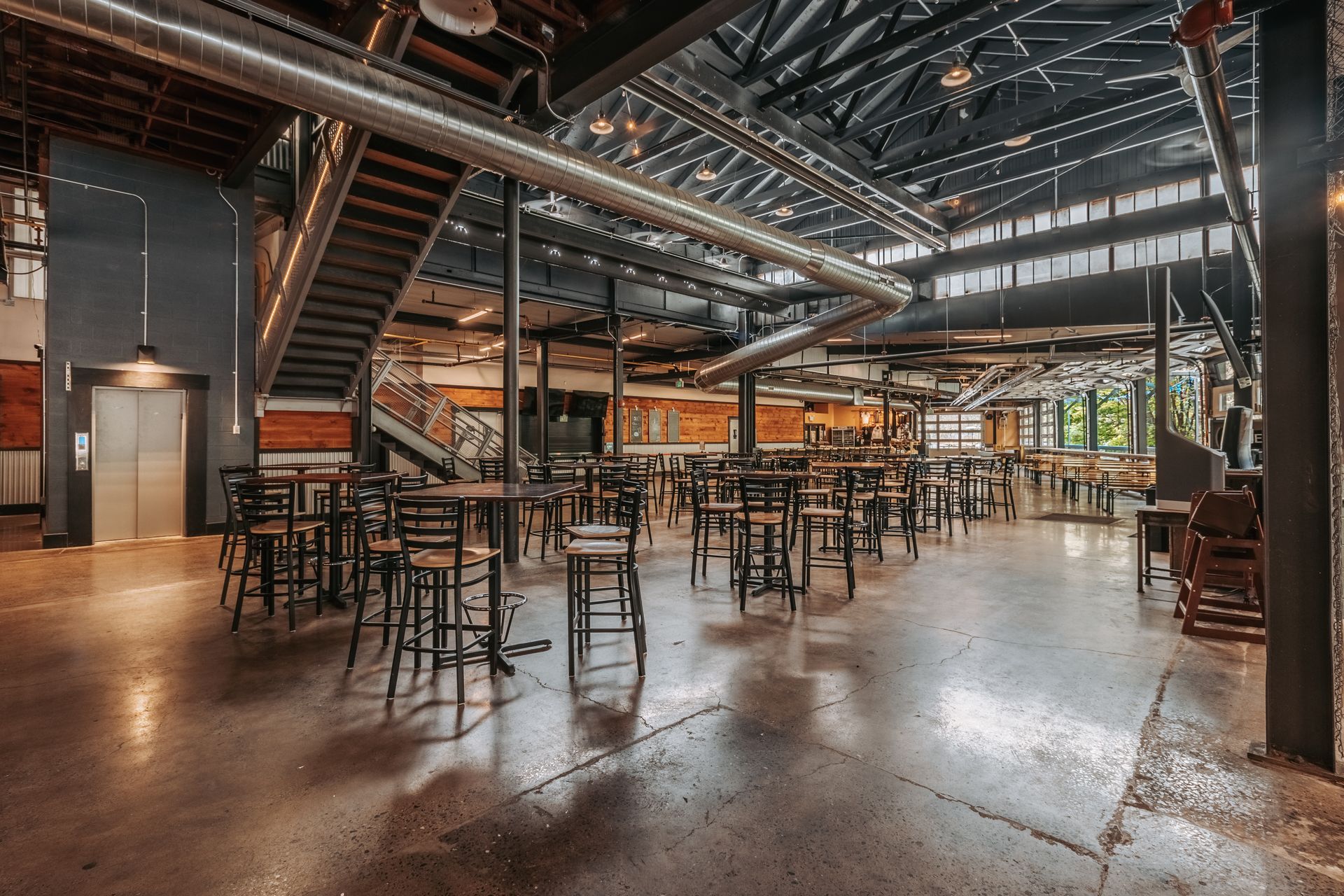 Axemann Brewery's hall with metal tables, high stools, and warm overhead lighting