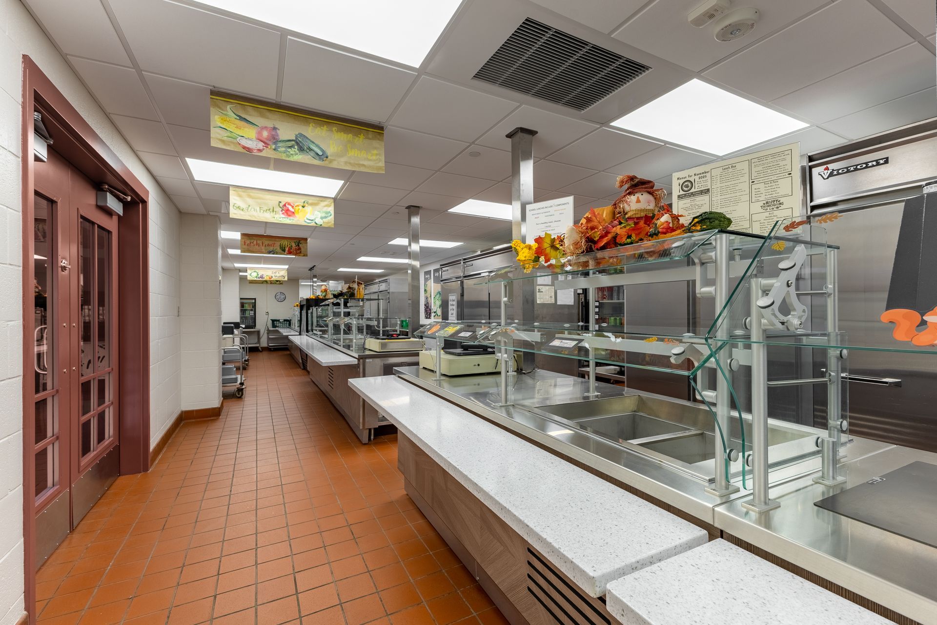 Mount Nittany Middle School Cafeteria with stainless-steel serving counter, tiled floor, and colorful hanging decorations