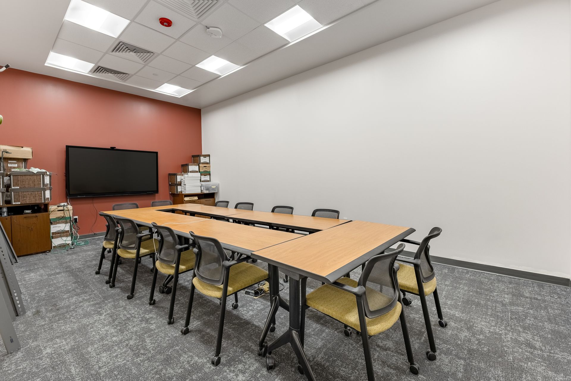 State College Area School District North Building's conference room with a long table, black chairs, wall-mounted TV, and fluorescent ceiling lights.