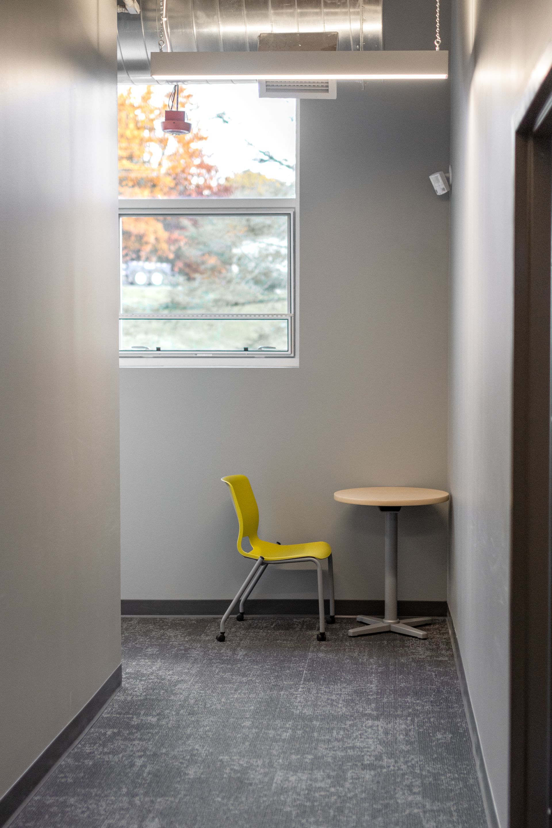 State College Area School District North Building's small office alcove with a yellow chair, round table, window, and exposed ductwork.
