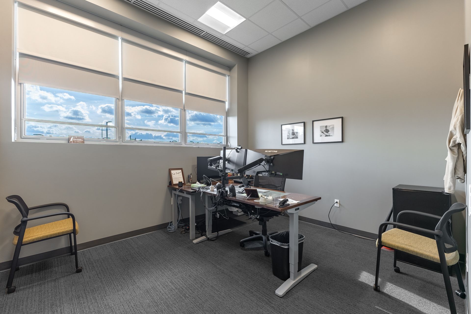 State College Area School District North Building's modern office with desk, computer equipment, two black chairs, carpeted floor, and windows with blinds.