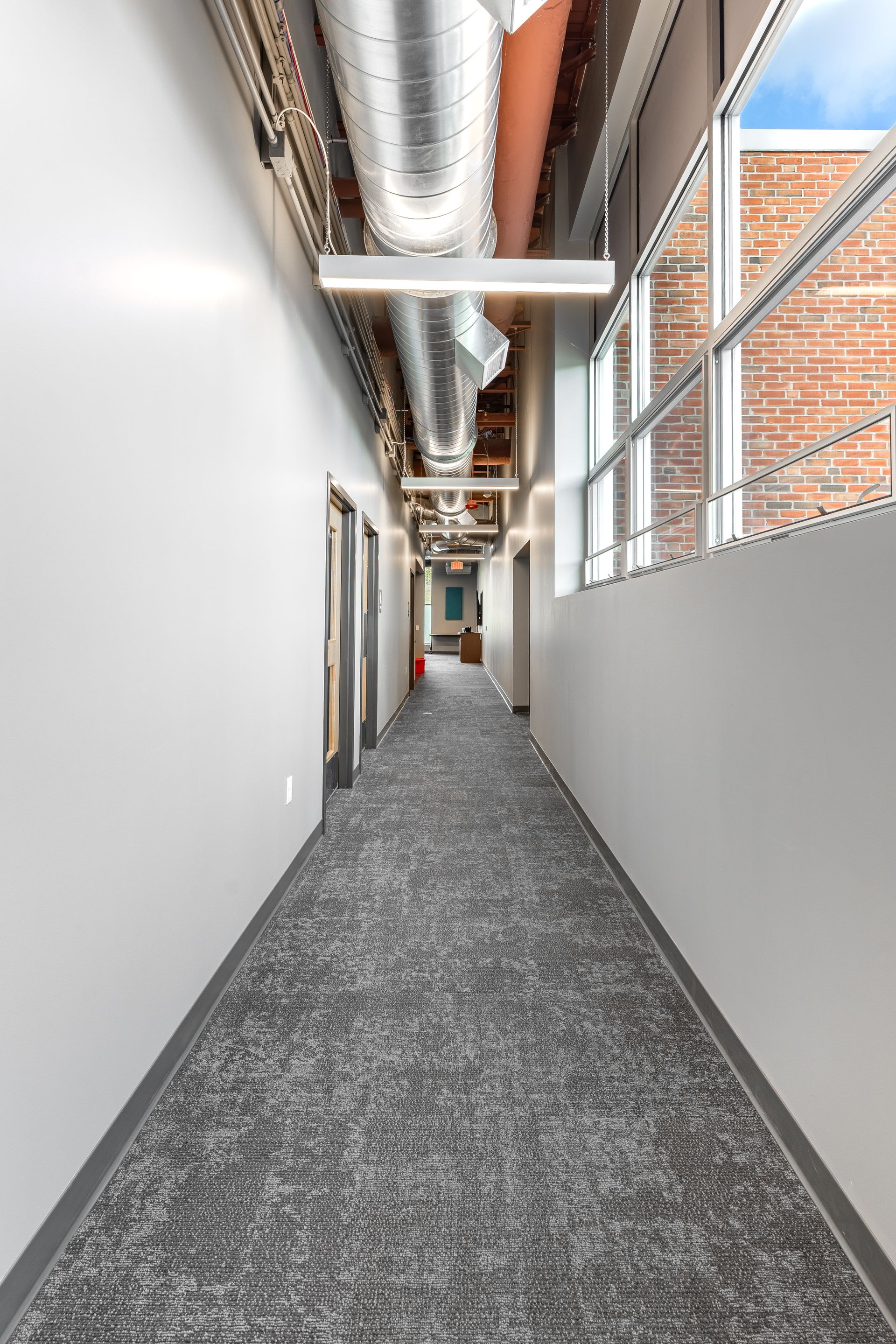 State College Area School District North Building's office hallway with gray carpet, white walls, exposed ductwork, and windows on the right