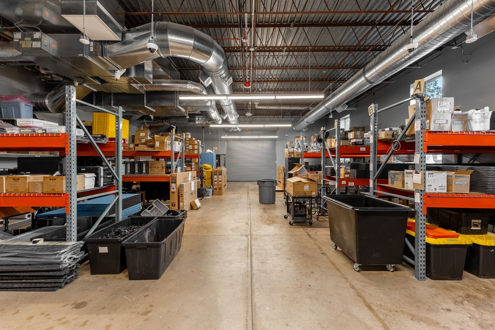 State College Area School District North Building's warehouse aisle with metal shelving, stacked boxes, and exposed ductwork under bright industrial lighting