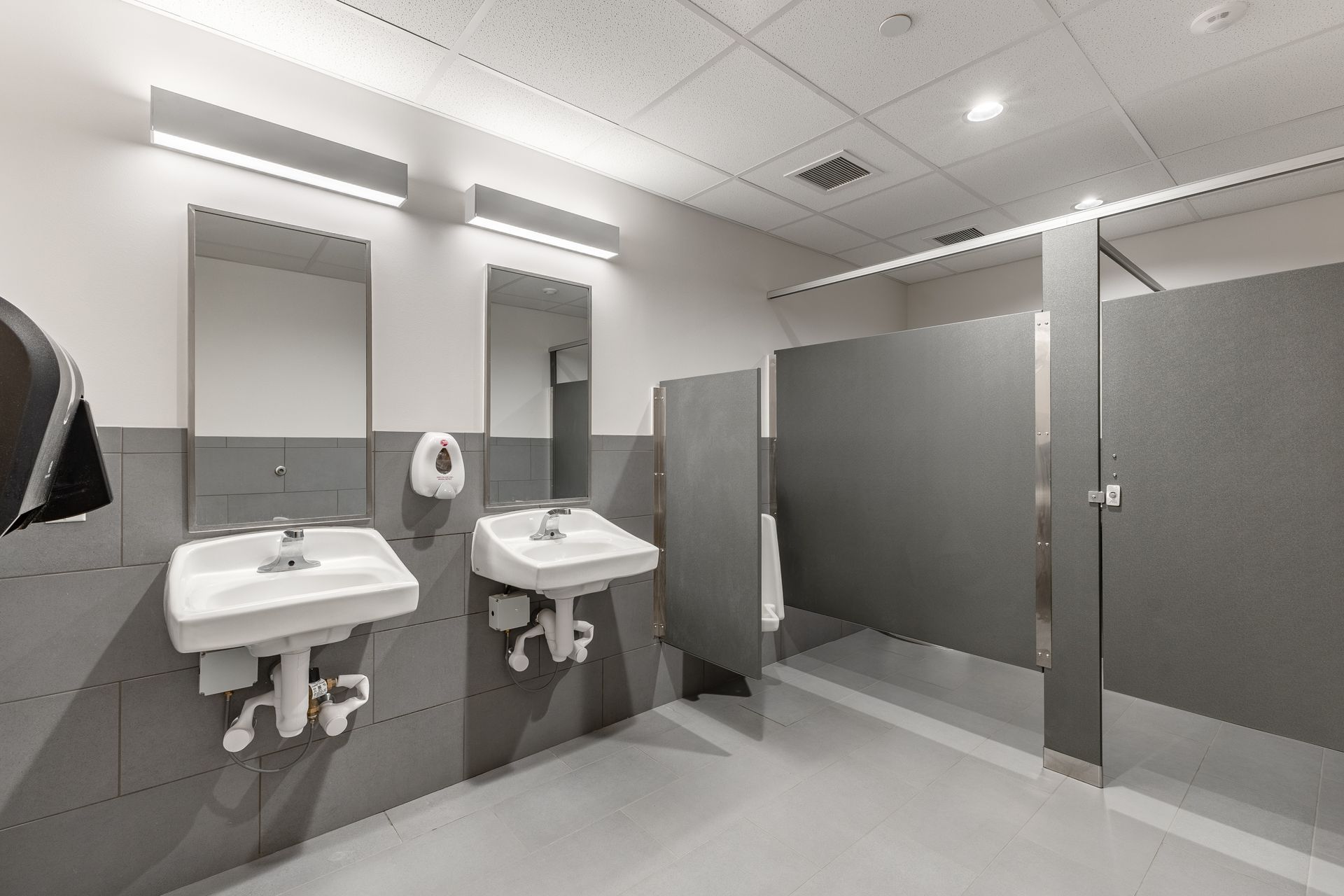 State College Area School District North Building's restroom with sinks, mirrors, and gray stall partitions under bright ceiling lights.