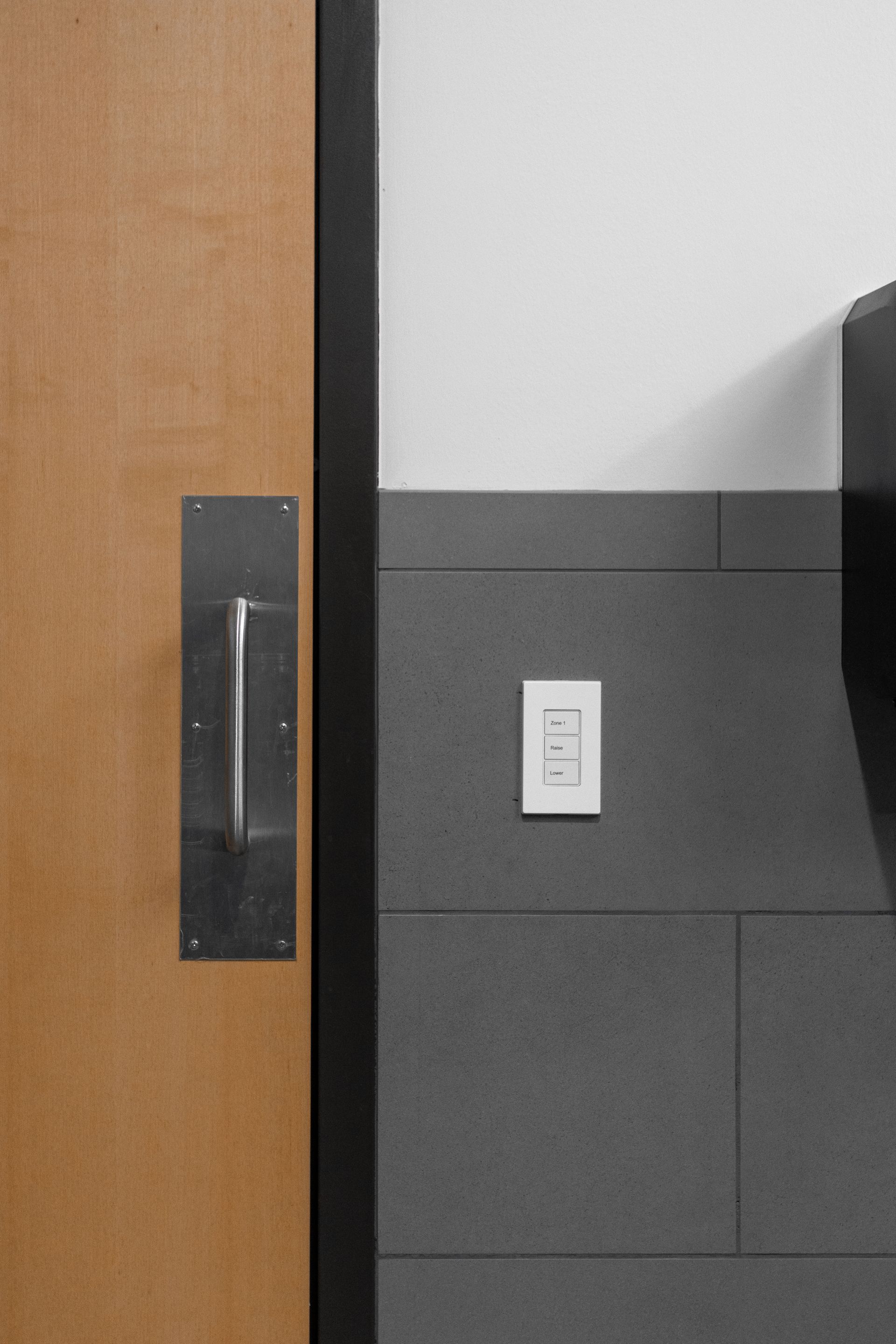 State College Area School District North Building's wooden door with a vertical metal handle beside a gray tiled wall and a light switch panel.