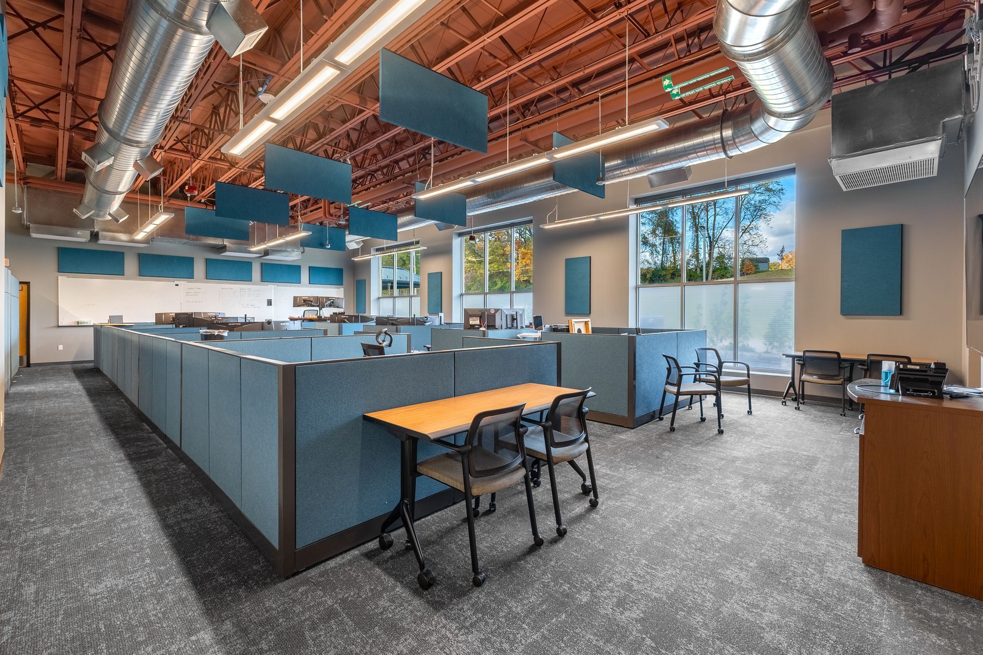 State College Area School District North Building lounge with blue cubicles, desks, stools, and exposed ductwork under warm ceiling lights