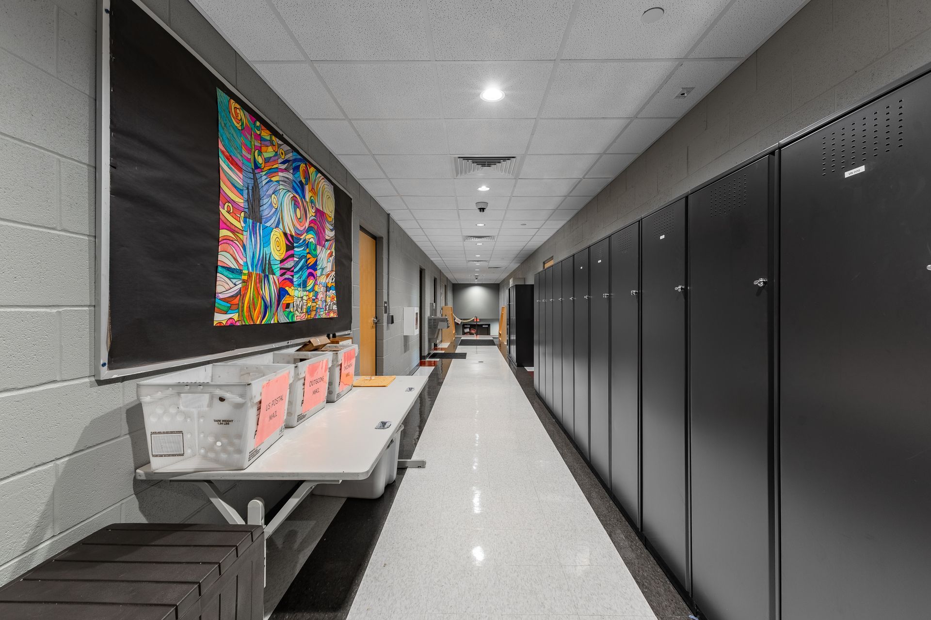 State College Area School District North Building's bright hallway with black lockers, gray benches, and a colorful wall display in a school or office setting
