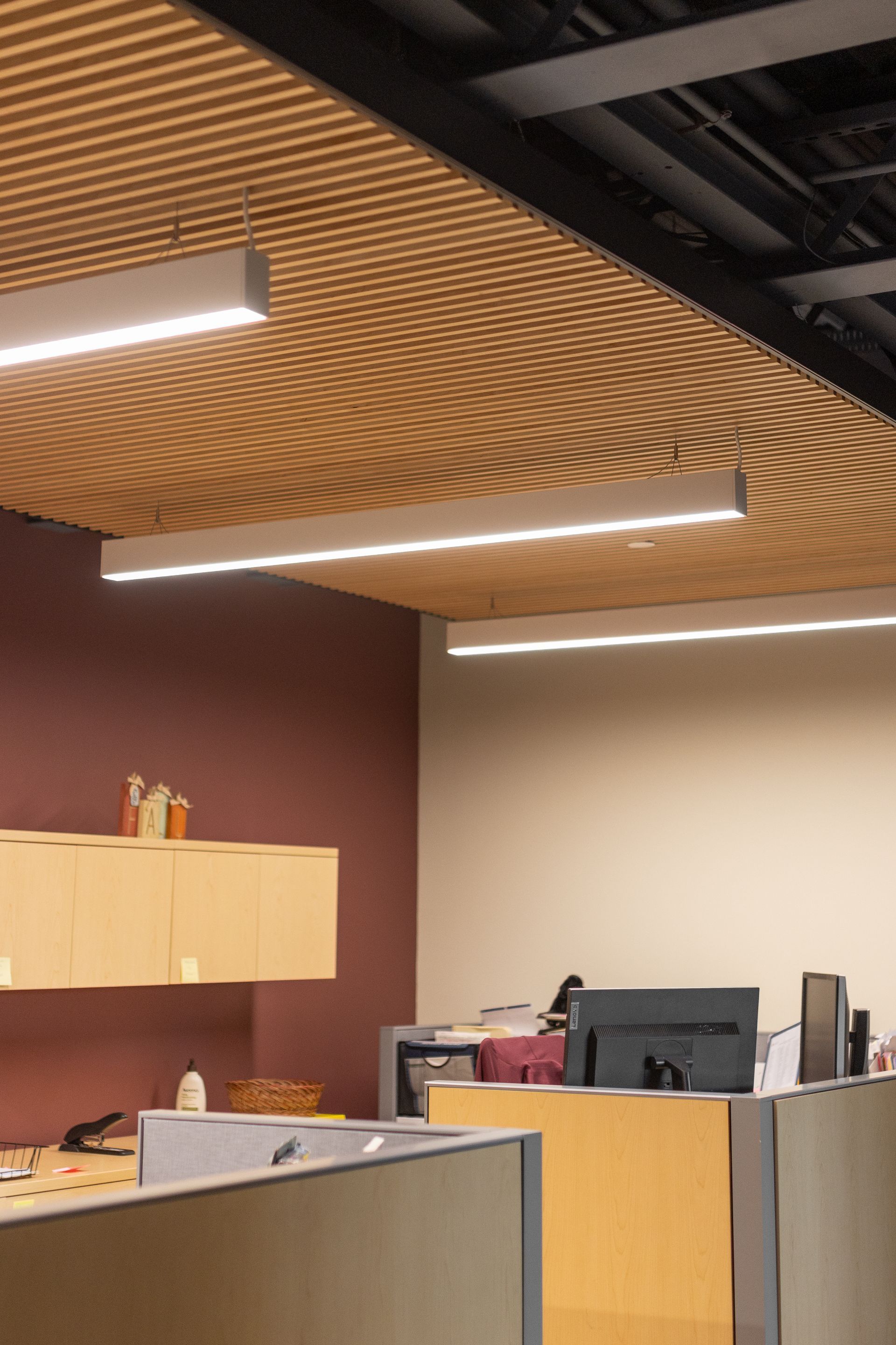 State College Area School District Panorama Village building's modern office reception area with wood-slat ceiling, pendant lights, and a front desk with a monitor