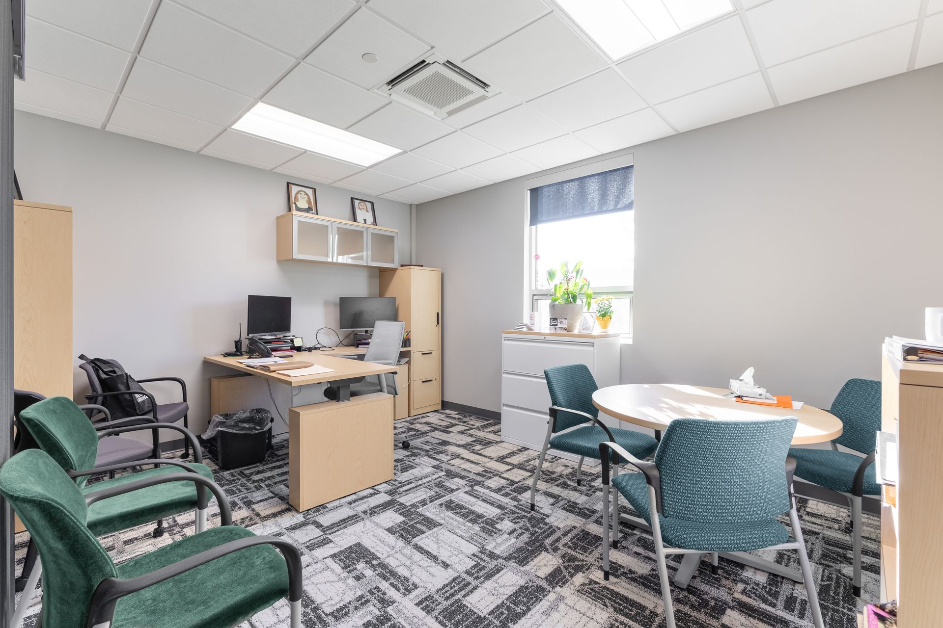 State College Area School District Panorama Village building's small office with desks, computer monitors, chairs, and a window with plants and daylight.