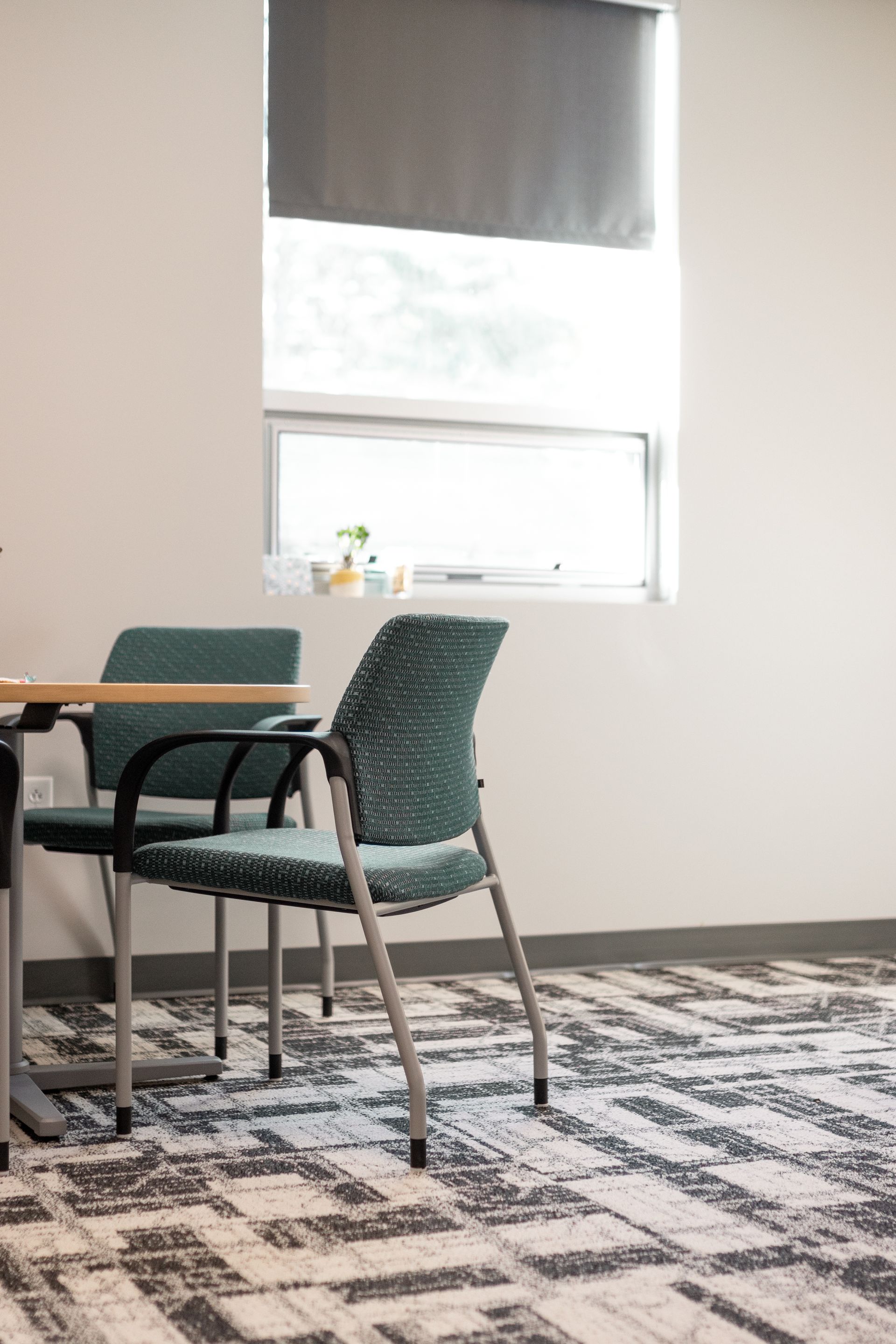 State College Area School District Panorama Village building's small dining area with teal chairs, table by a window, and patterned carpet