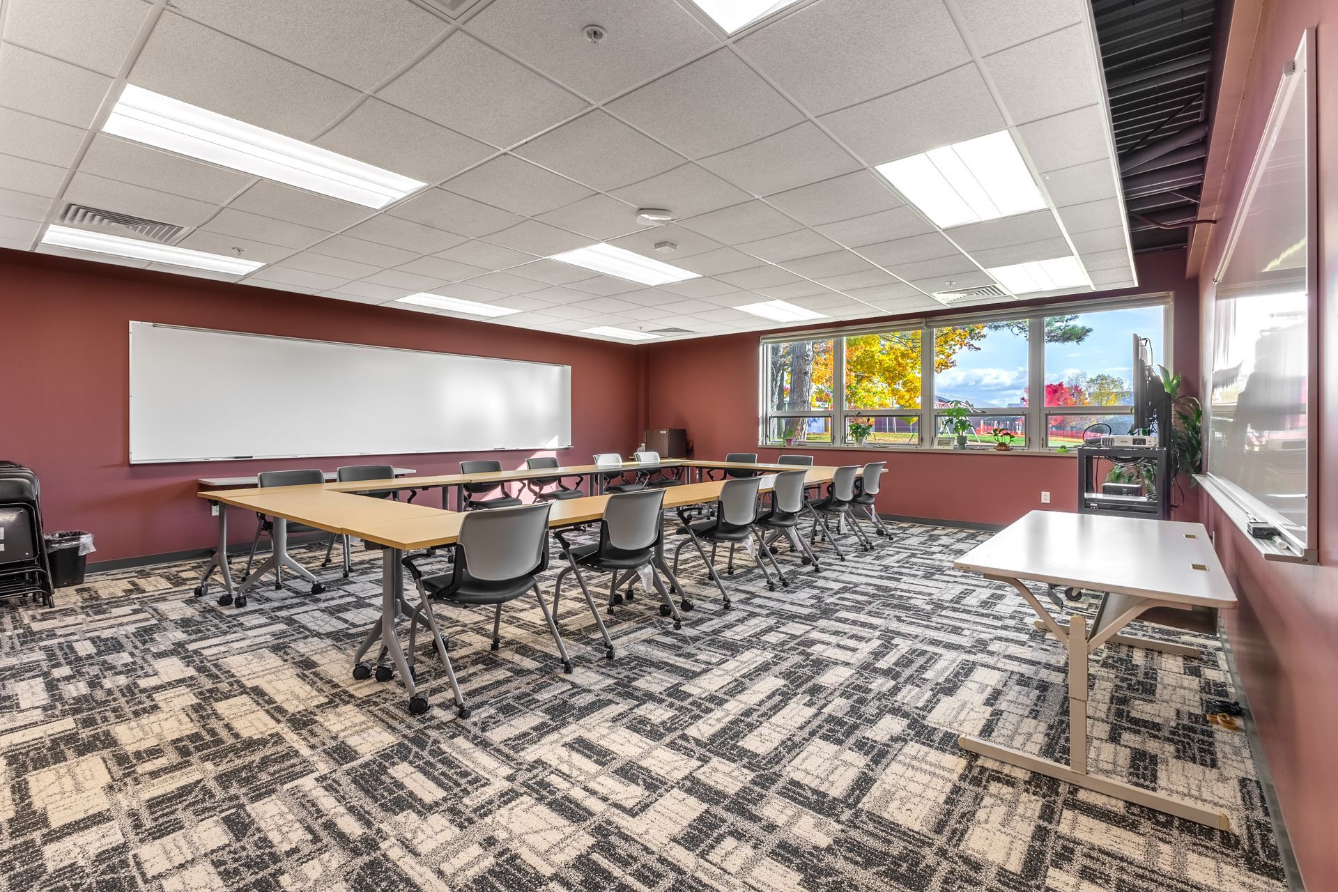 State College Area School District Panorama Village building's empty conference room with tables, chairs, whiteboard, and large windows overlooking trees