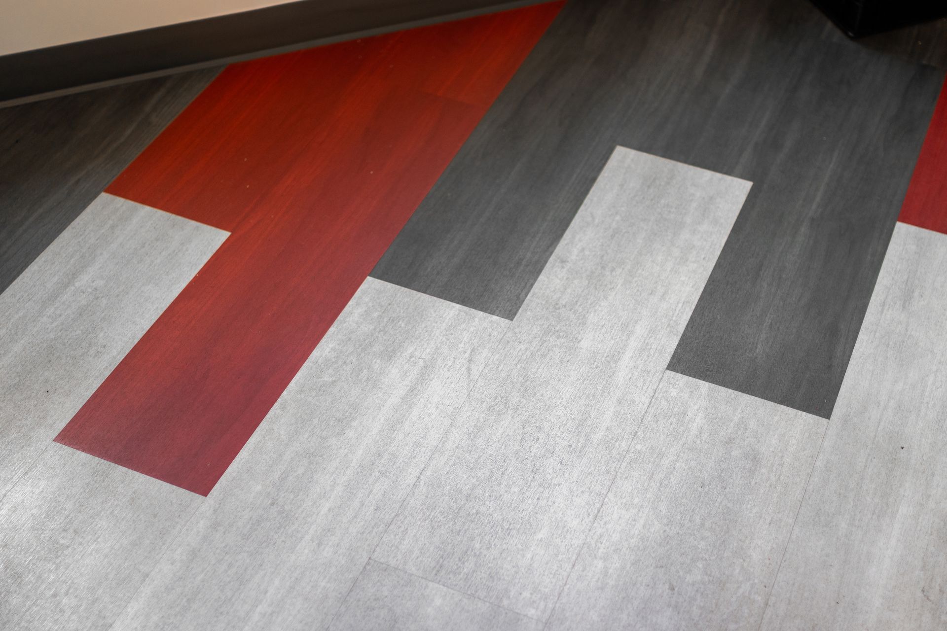 State College Area School District Physical Plant Building's abstract geometric floor with red, white, and gray angular stripes on a textured surface