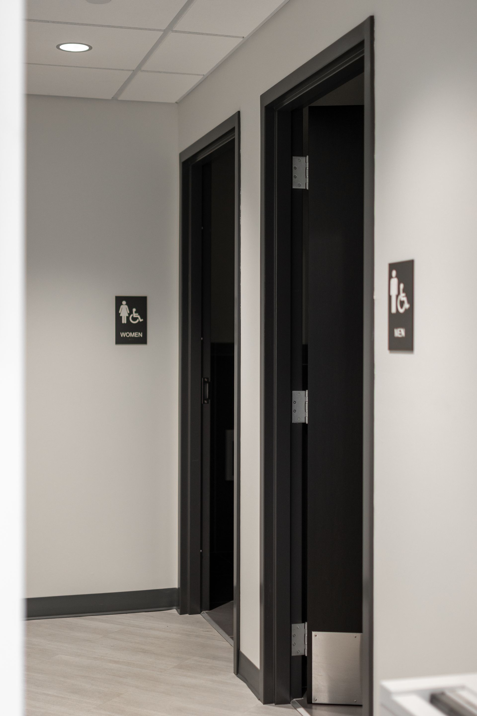 State College Area School District Physical Plant Building's hallway with two black restroom doors and wall signs on light gray walls.