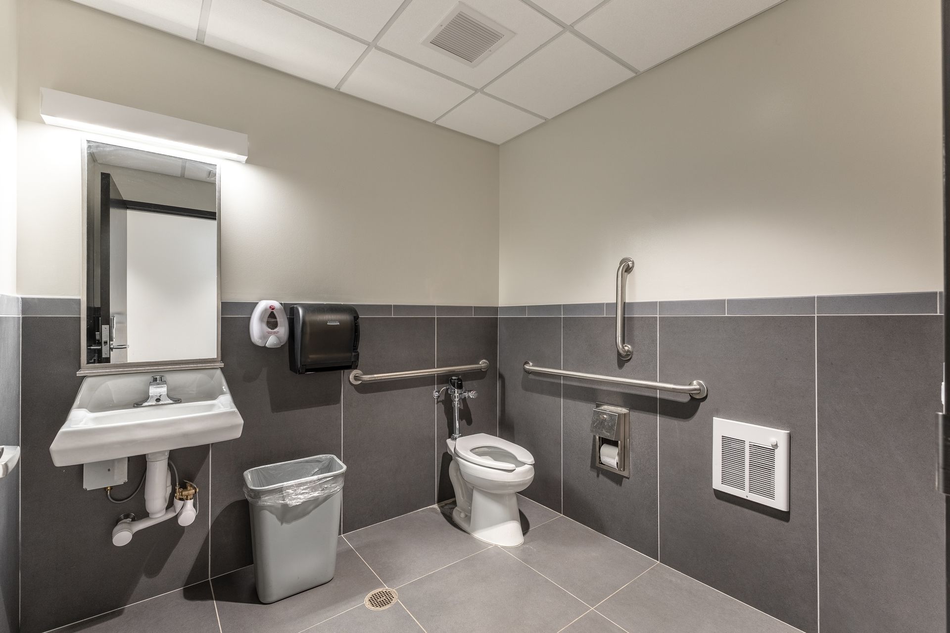 State College Area School District Physical Plant Building's accessible restroom with sink, mirror, toilet, grab bars, and gray tile walls