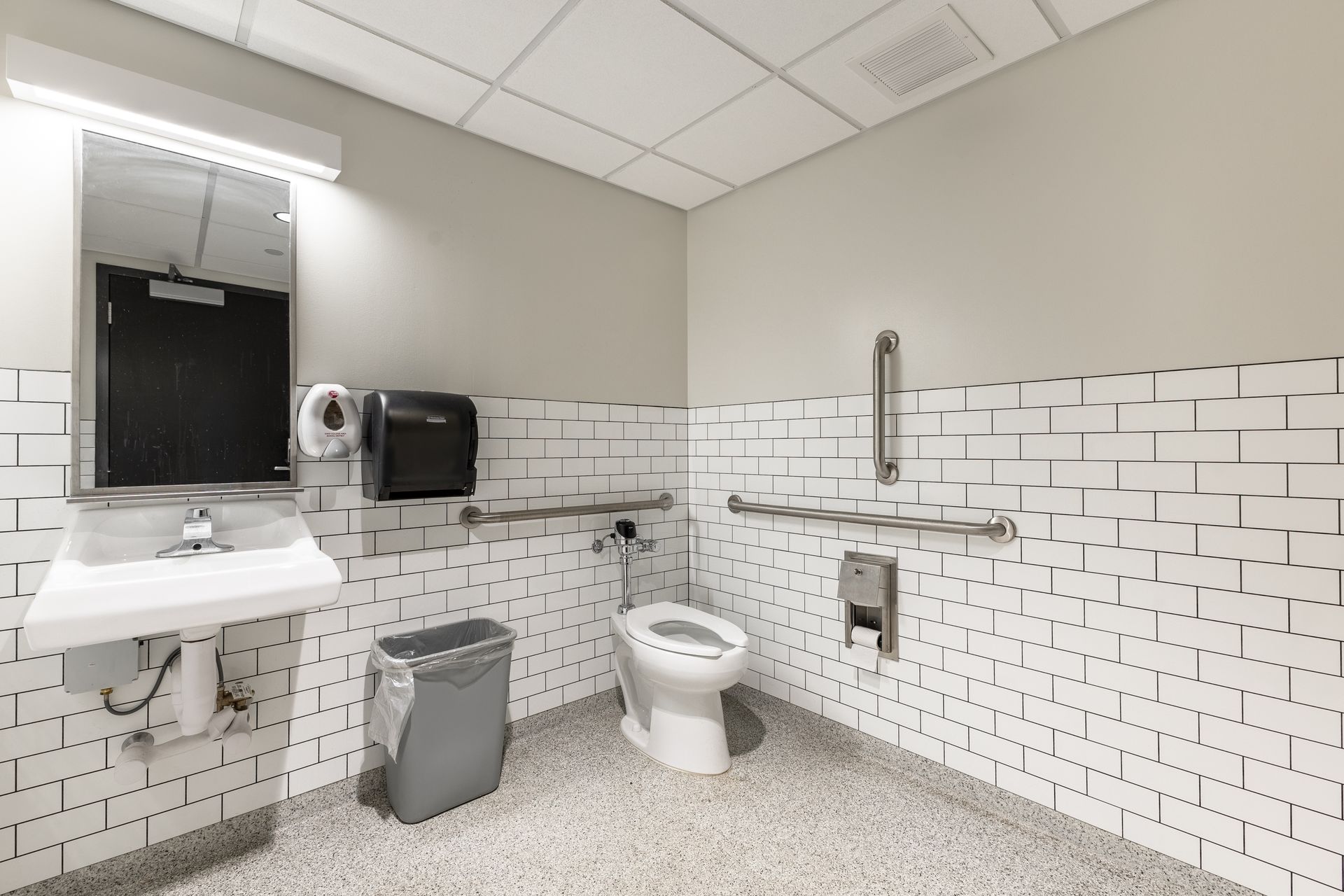 State College Area School District Physical Plant Building's accessible restroom with sink, mirror, toilet, grab bars, and white tiled walls