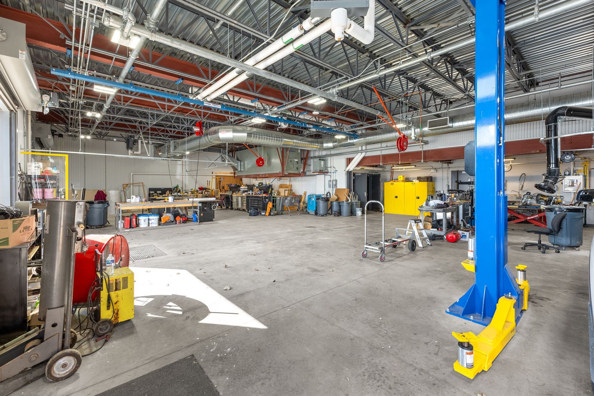 State College Area School District Physical Plant Building's workshop with machinery, tool carts, and a blue overhead lift inside a high-ceilinged warehouse.
