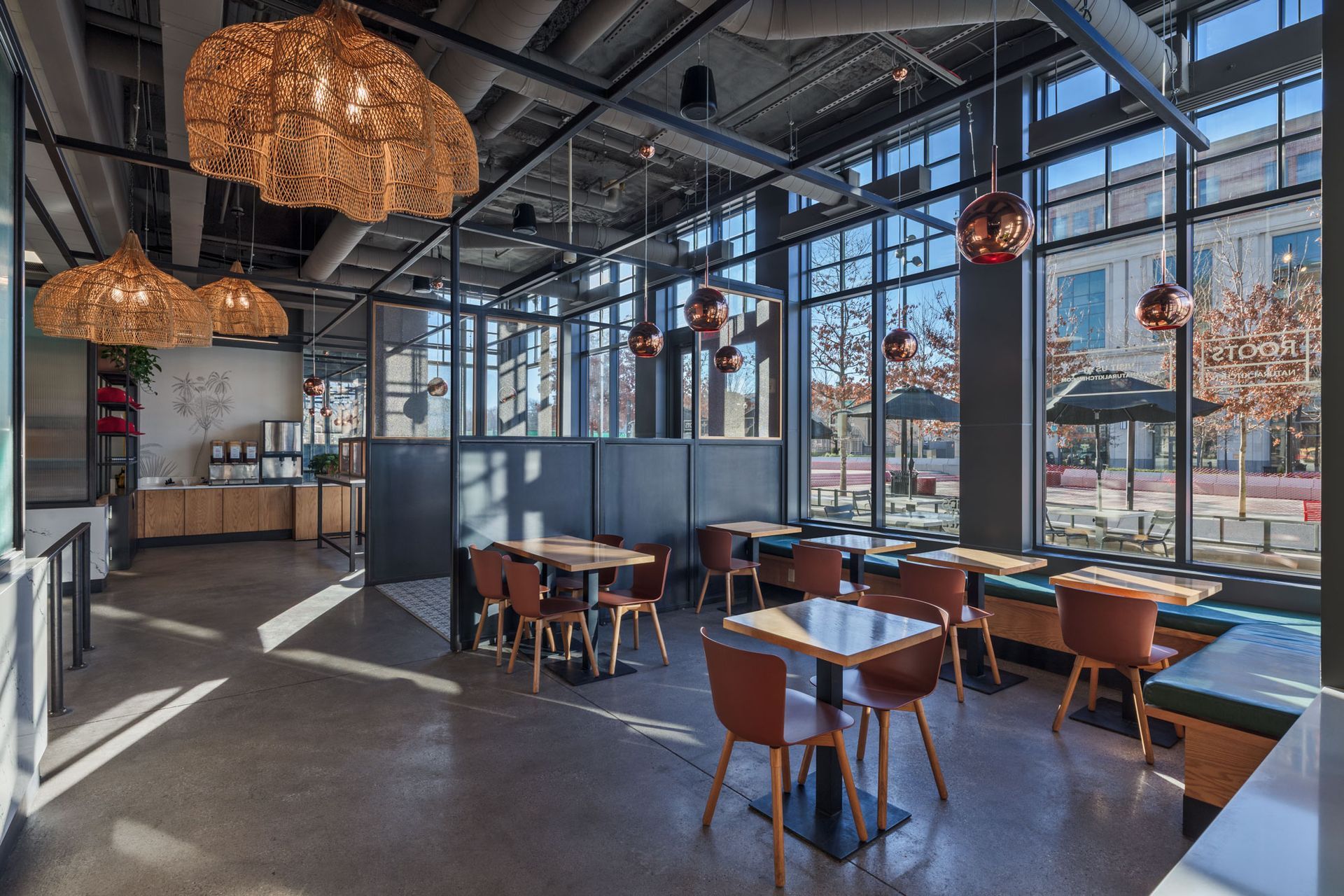 Roots Natural Kitchen interior with wooden tables, brown chairs, woven pendant lights, and floor-to-ceiling windows.