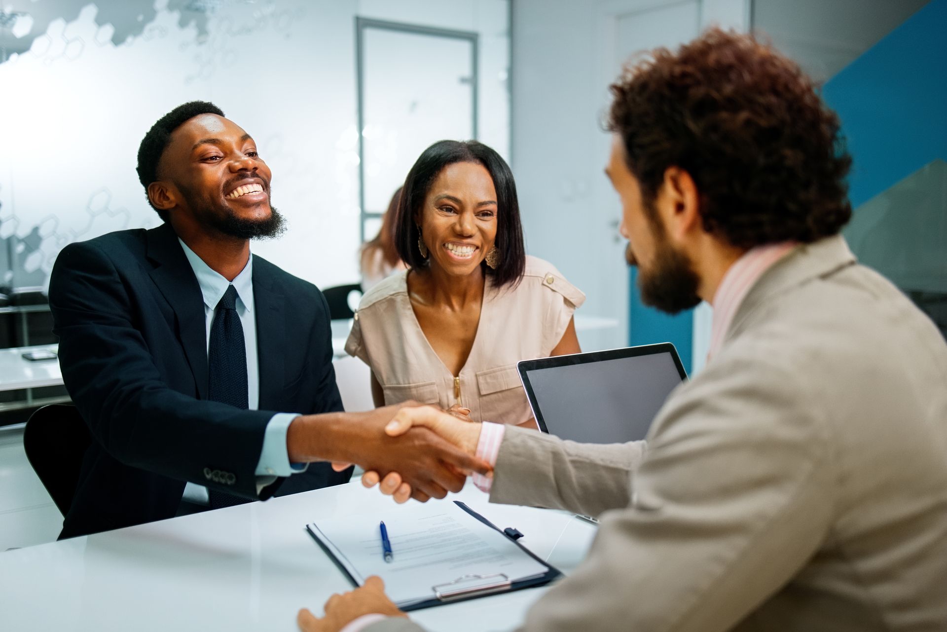 Couple shaking hands with a professional at a desk, smiling.