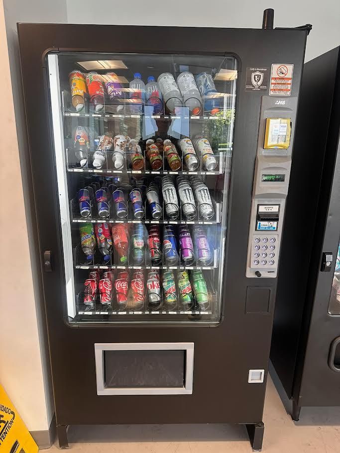 Blue-lit vending machine filled with assorted drinks, with payment keypad on the right and push door below