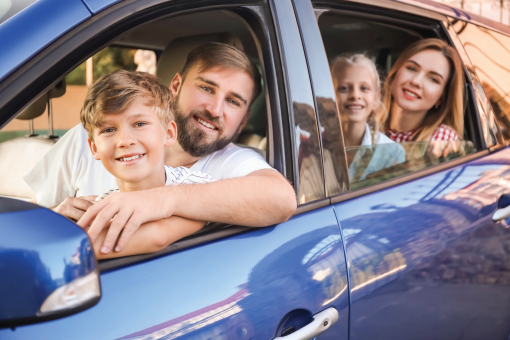 A smiling family of four sitting inside a blue car, looking out the windows.