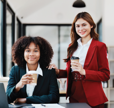 A woman in an apron is holding a tablet in front of a welcome open sign.