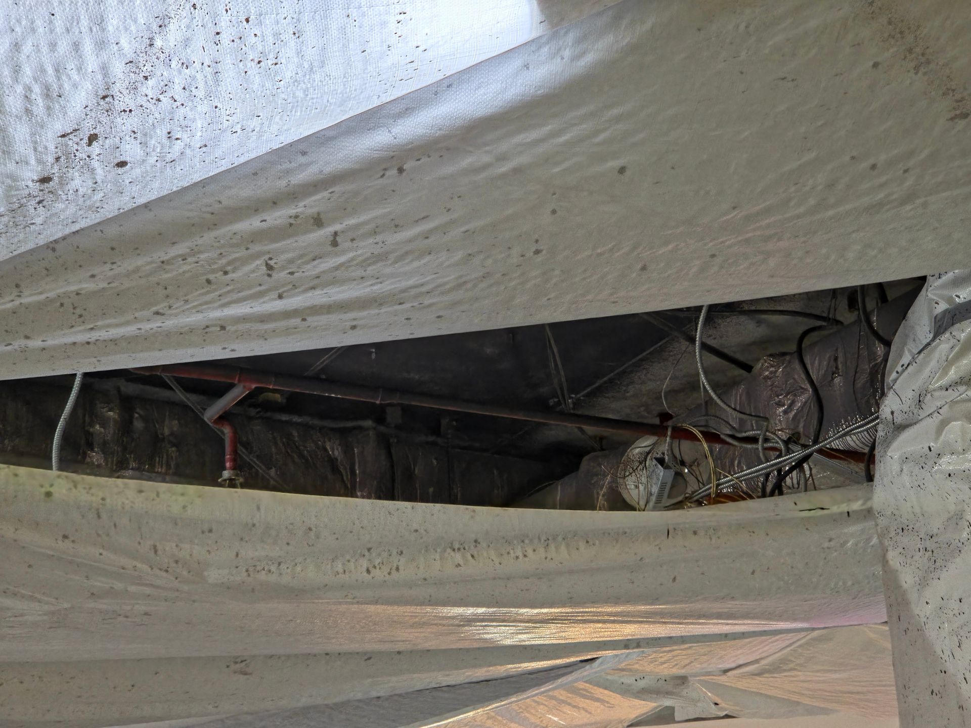A view inside a crawl space showing a white vapor barrier covering utility pipes overhead. A view inside a crawl space showing a white vapor barrier covering utility pipes overhead.