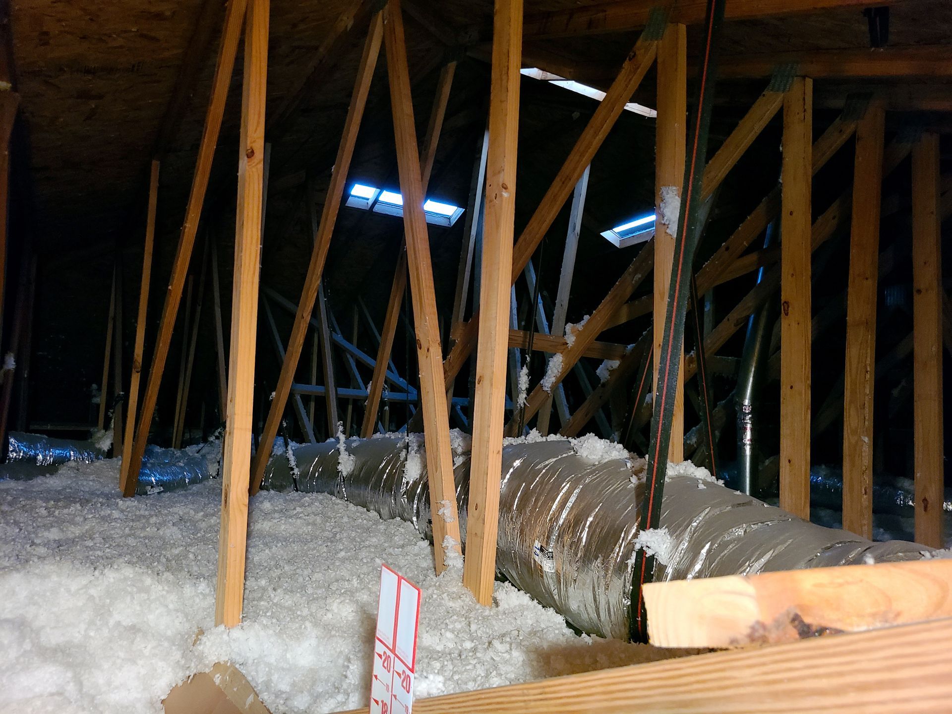 A crawlspace with wooden beams, loose insulation, and a large duct running through the area.