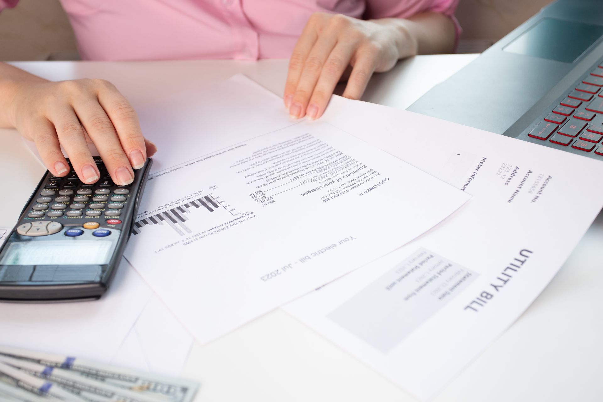 A partial view of a woman at home counting utility bills on a calculator.