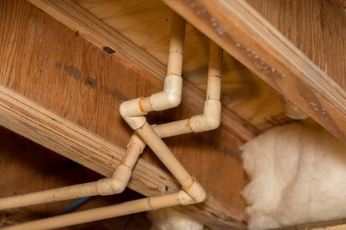 Aged and yellowed water PVC pipes inside a house’s crawlspace.