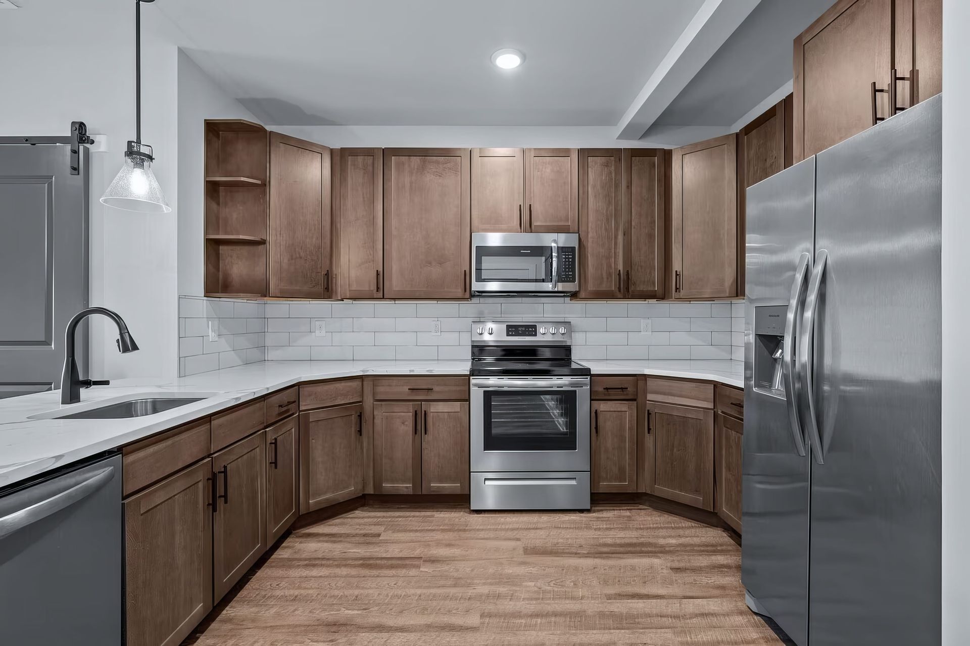 Spacious modern kitchen in high-end rental apartment with marble countertops, wood cabinetry, refrigerator, microwave, stove and oven