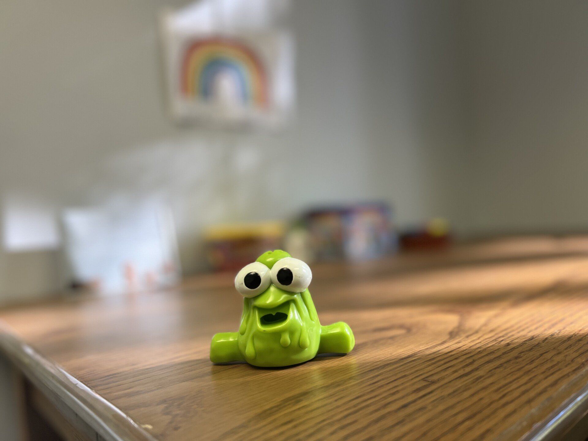 A green toy with big eyes is sitting on a wooden table.