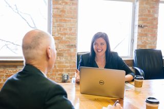 woman smiling in front of laptop at man sitting across desk