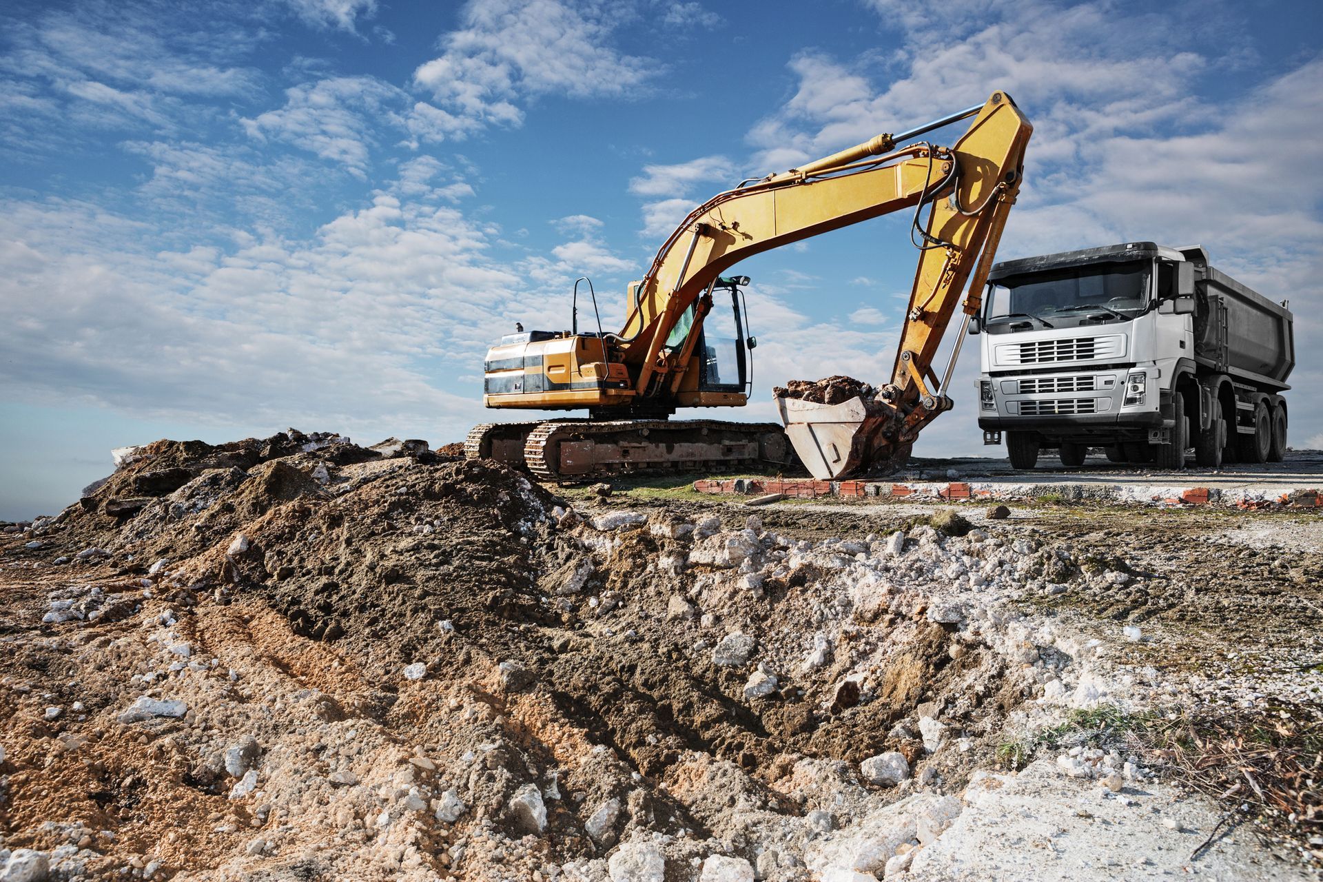 Excavator bucket scooping earth, against a sky with pink and blue clouds.
