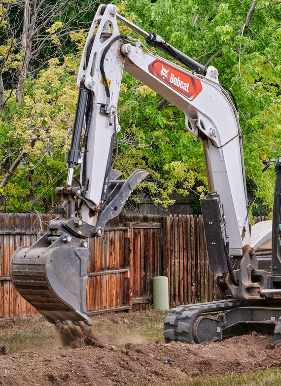 Pipeline being installed in a trench by yellow construction equipment, in a forest, at sunset.