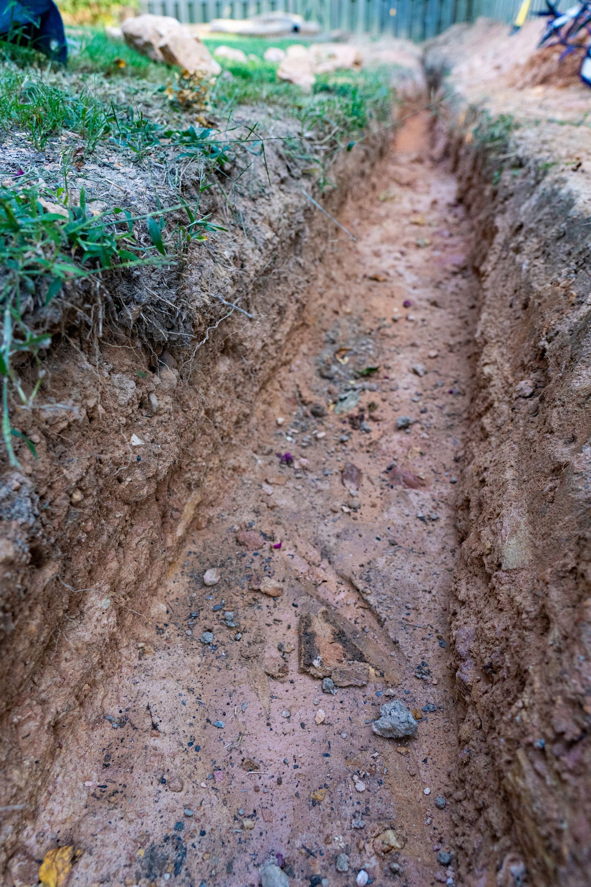 A narrow trench dug in the ground, surrounded by grass and dirt.