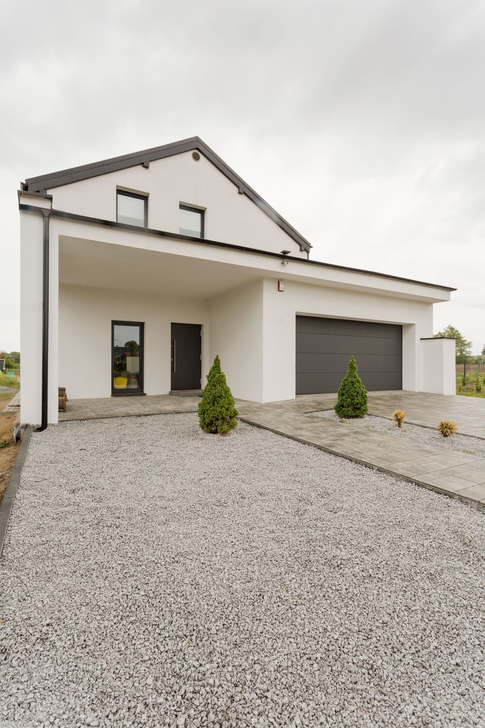 White modern house with gravel driveway, gray garage door, and entry overhang.