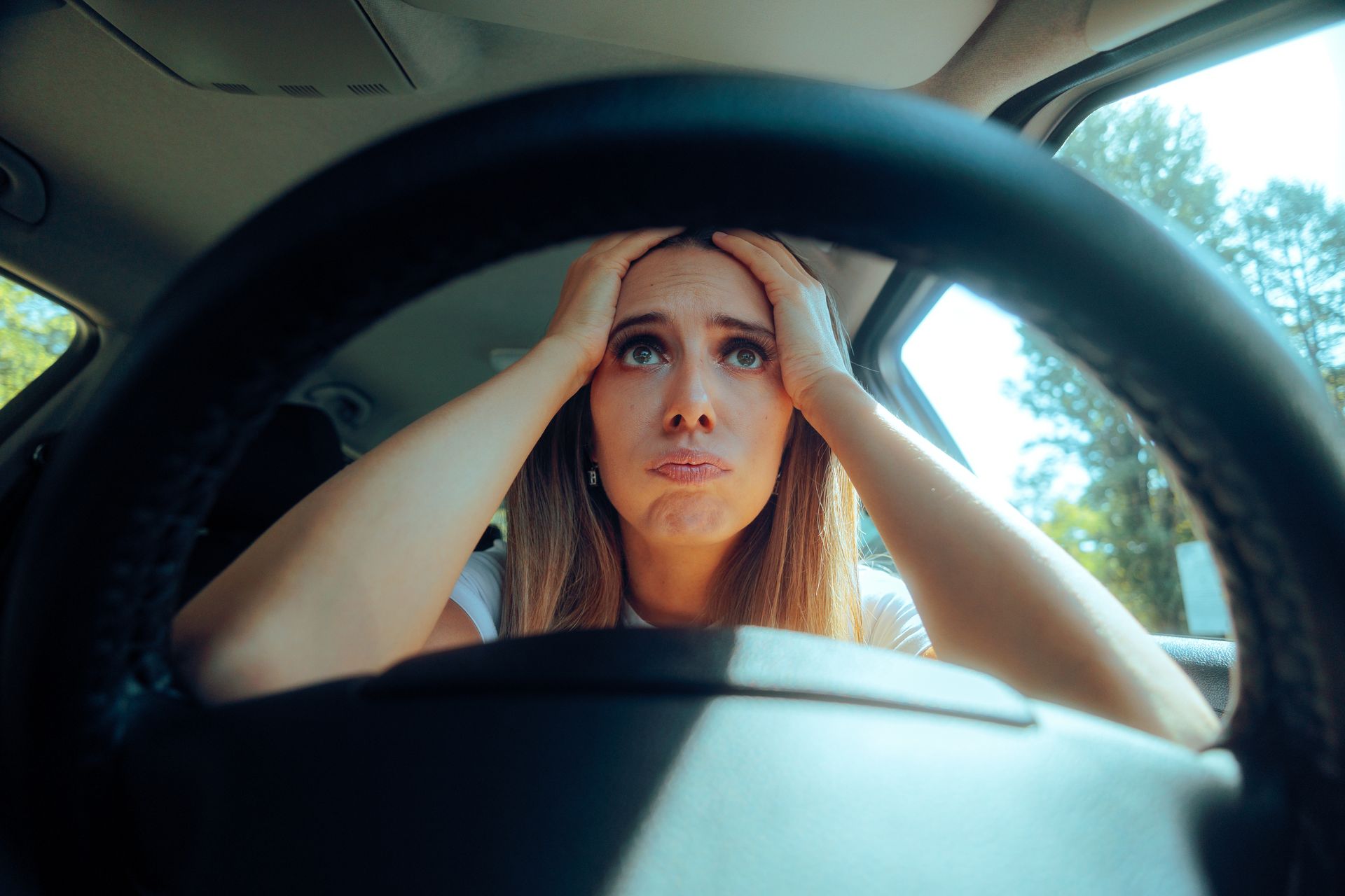 Woman in car, hands on head, looking stressed through steering wheel. Woman in car, hands on head, looking stressed through steering wheel.