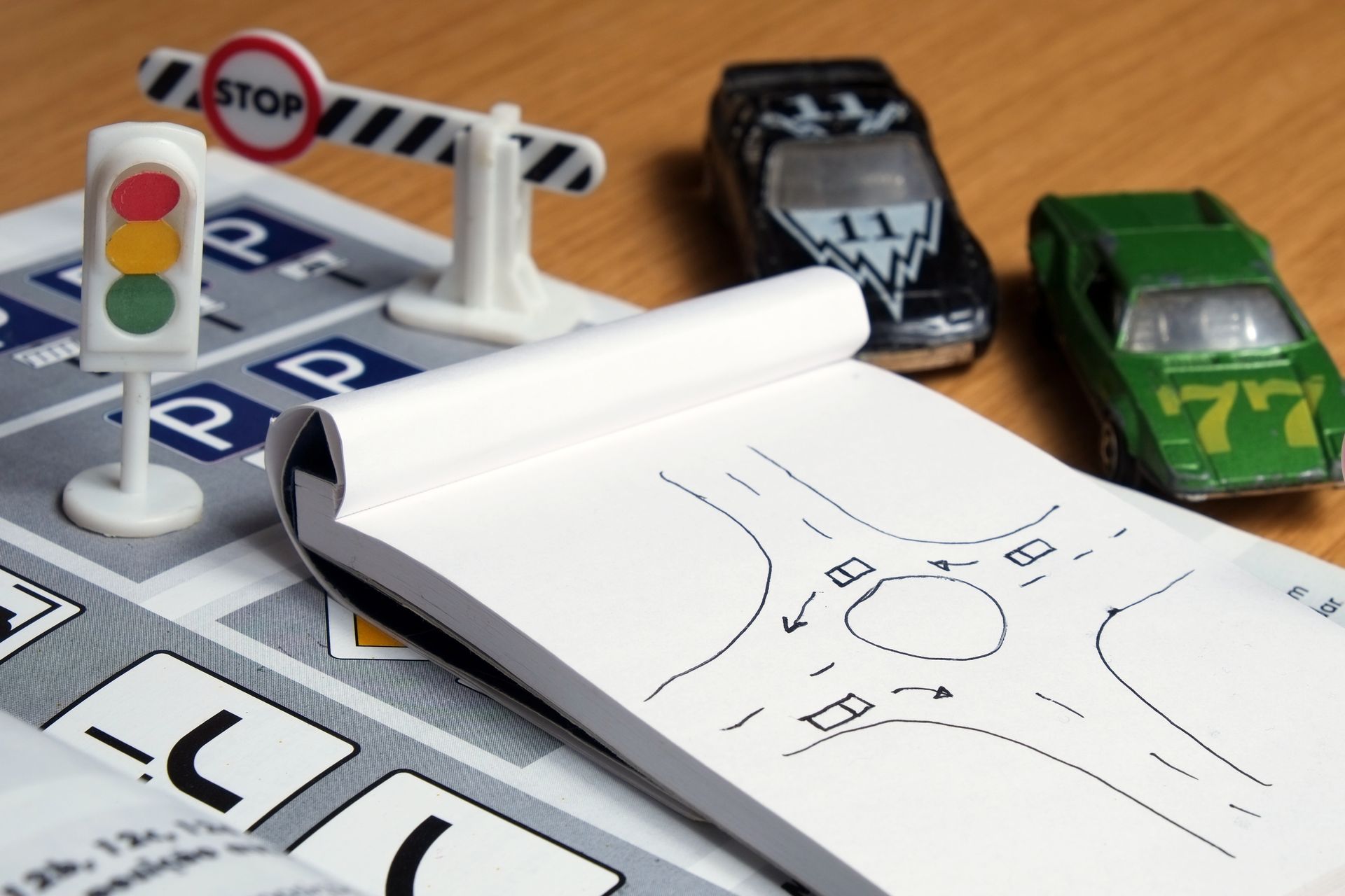 Driving lesson setup with toy cars, traffic signals, and roundabout drawing on a notepad. Driving lesson setup with toy cars, traffic signals, and roundabout drawing on a notepad.