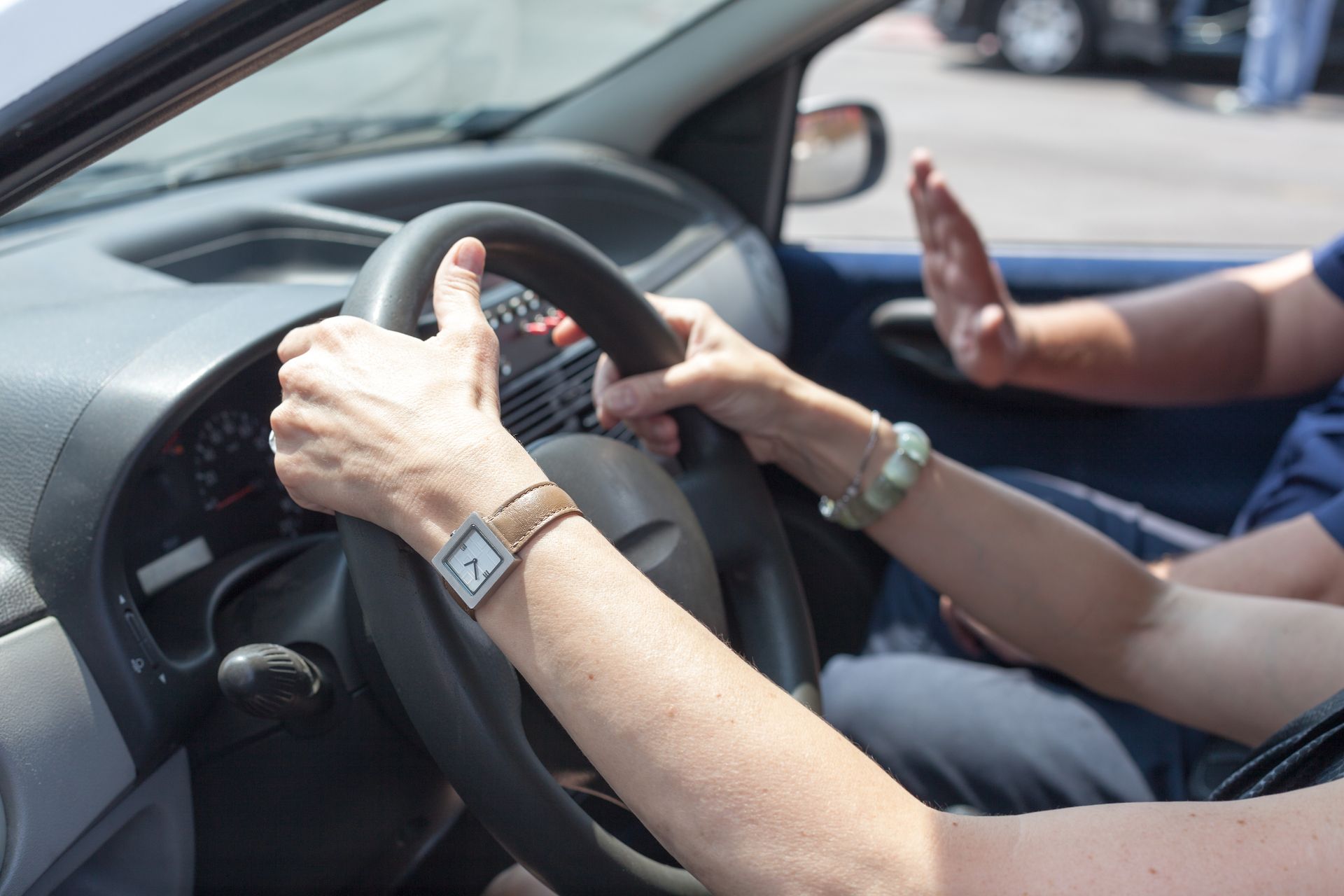 Hands on steering wheel; another hand raised in a car, presumably while driving.