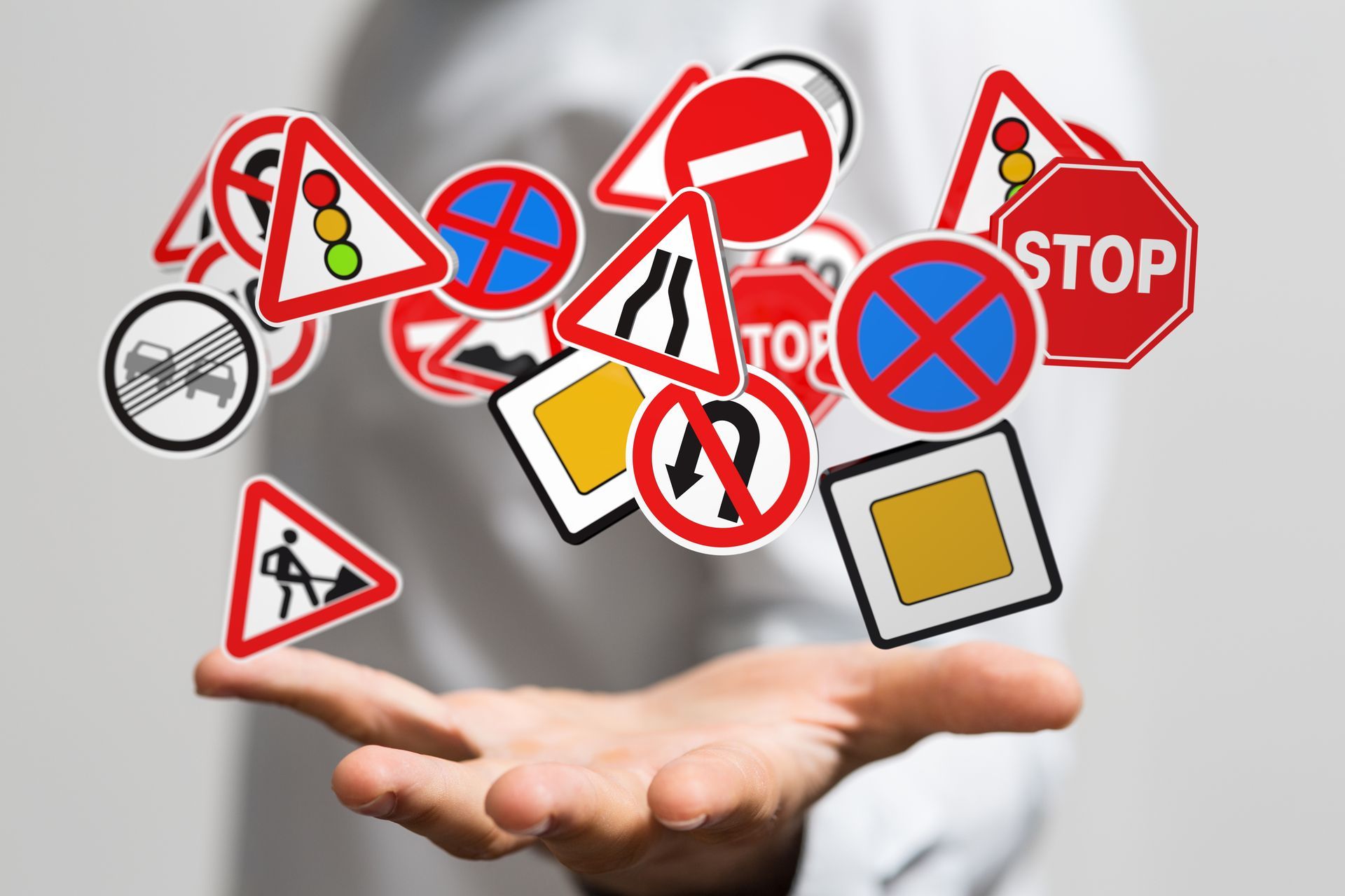 Person's hand holds up a collection of various floating road signs, including stop, no parking, and construction symbols. Person's hand holds up a collection of various floating road signs, including stop, no parking, and construction symbols.