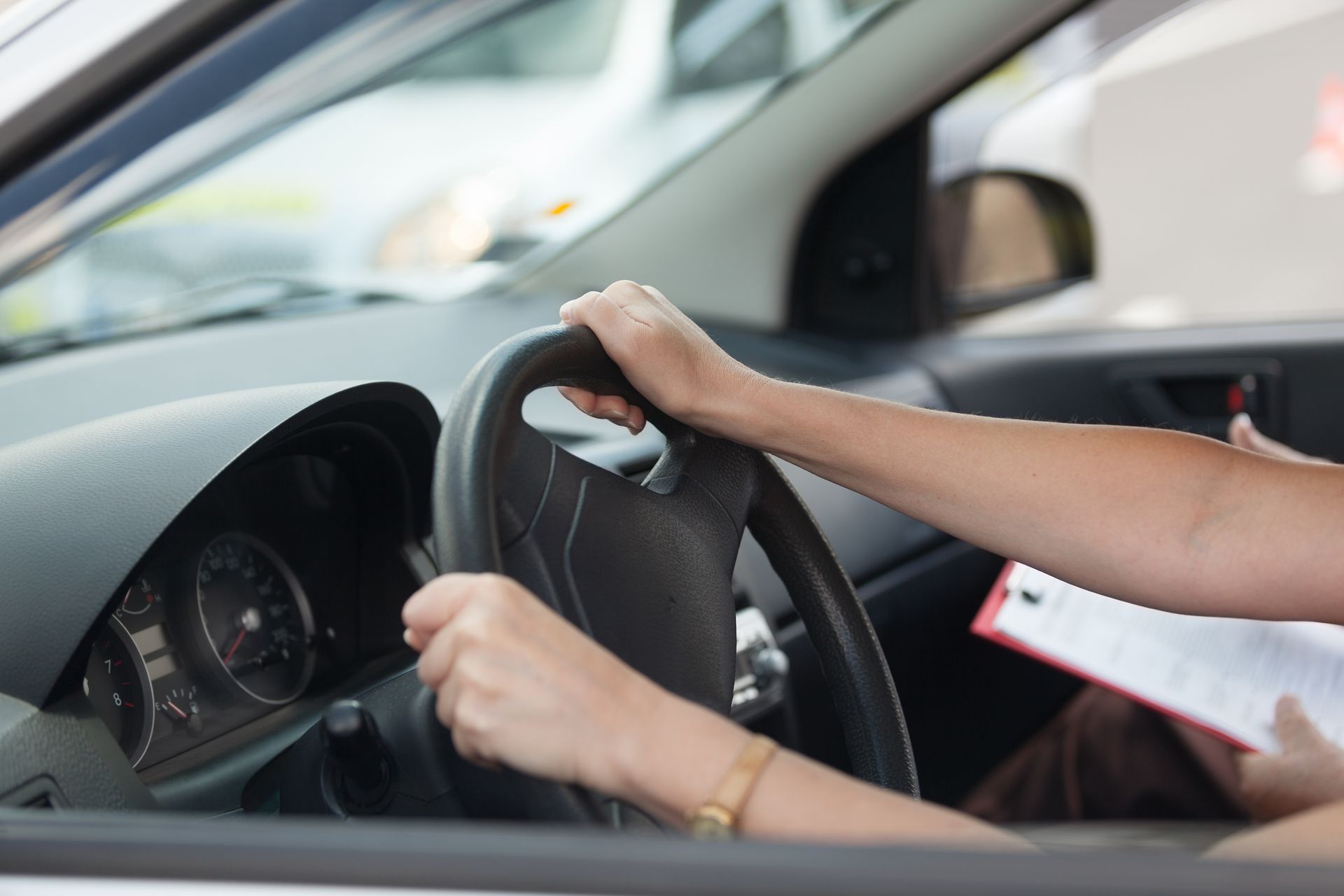 Hands gripping a steering wheel inside a car, with a clipboard in the passenger seat. Hands gripping a steering wheel inside a car, with a clipboard in the passenger seat.