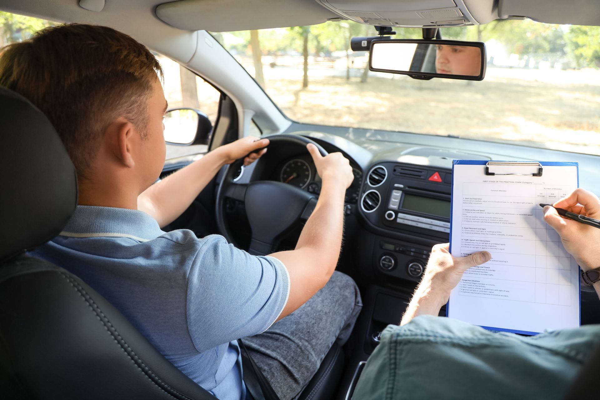 Man driving a car during a driving test, examiner taking notes on a clipboard.
