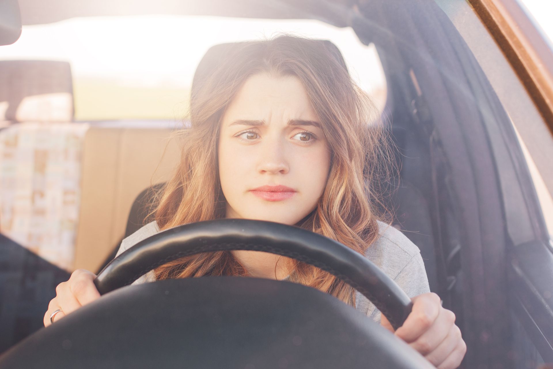 Woman gripping steering wheel with a worried expression, driving a car. Bright sunlight. Woman gripping steering wheel with a worried expression, driving a car. Bright sunlight.