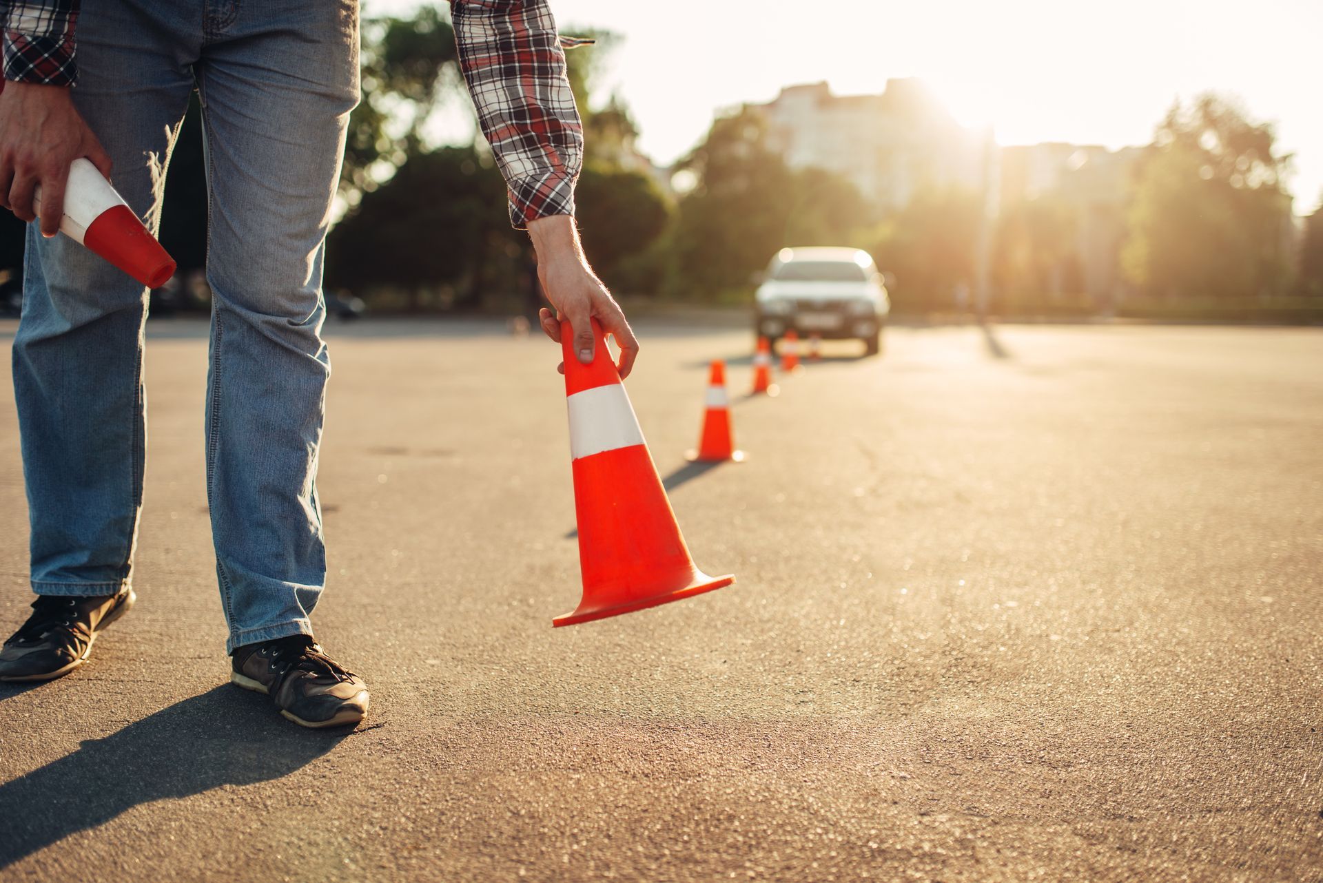 Person setting up orange traffic cones in an outdoor parking lot with a car in the distance.